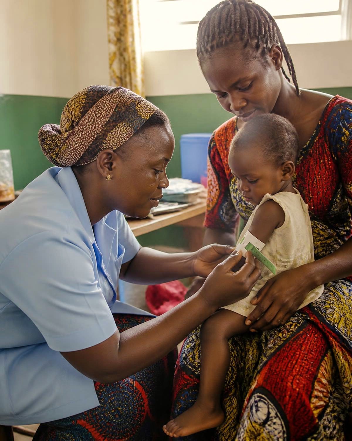 A nurse measures a baby's arm as the child sits on its mother's lap at a village health check