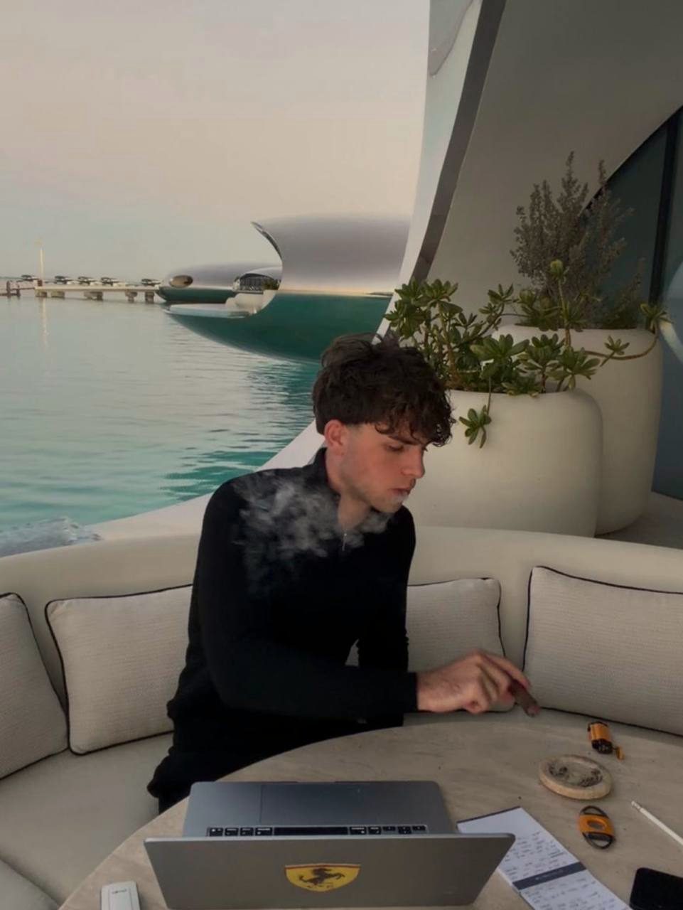 Max Thomas, founder of Vantage Concierge, working on a laptop on a sofa beside the water